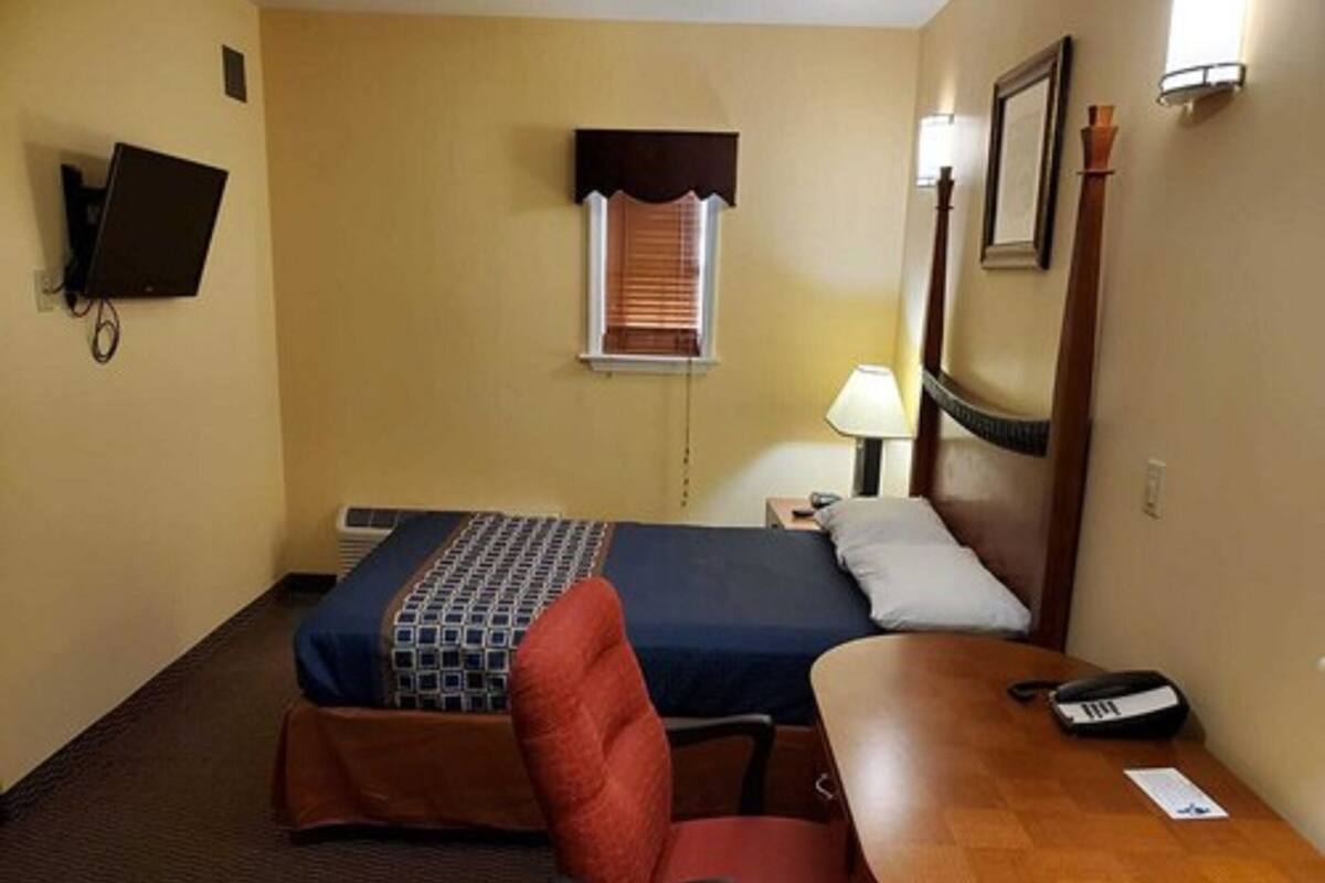Habitación de hotel con cama, escritorio, silla, lámpara, teléfono y televisor montado en la pared.