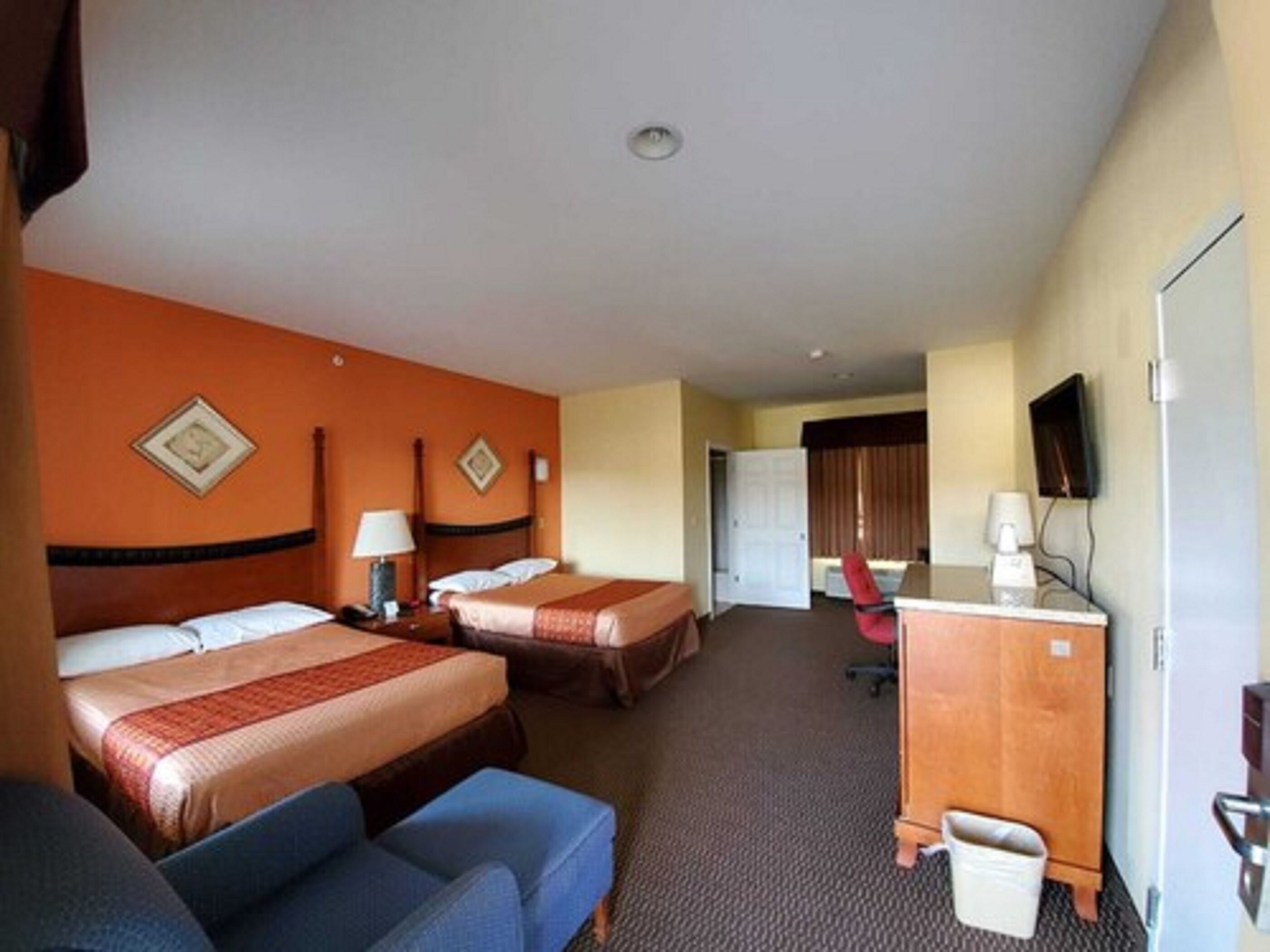 A hotel room with two beds, a desk, a chair, a television, and a trash bin.