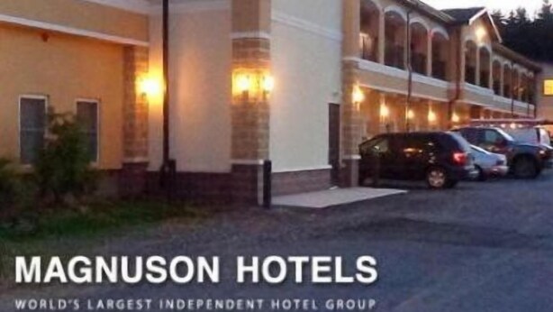 Um hotel com uma fileira de quartos, uma área externa coberta e um estacionamento.