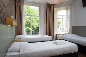 A hotel room with two single beds, a small desk with a chair, and a window with curtains. - Hotel Amsterdam Inn - Digital Access (Amsterdam)