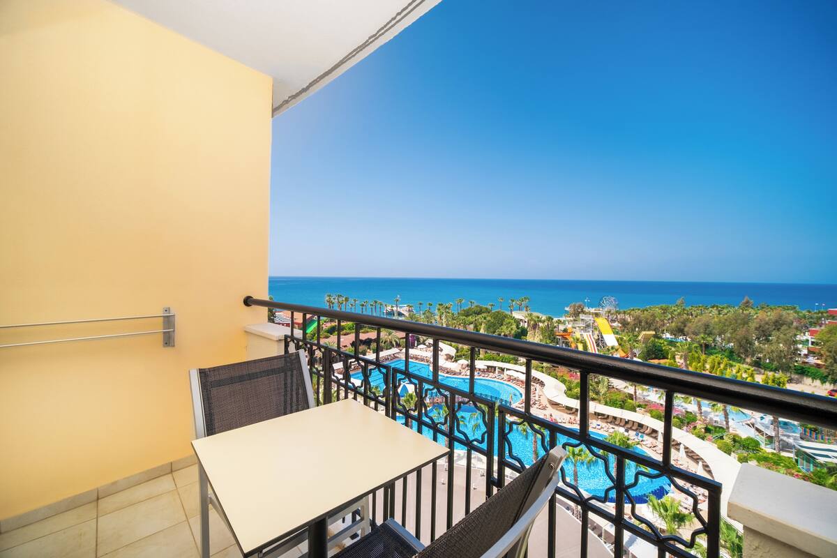 Un balcón con una mesa y una silla, con vista a un área de piscina y una vista despejada del océano.