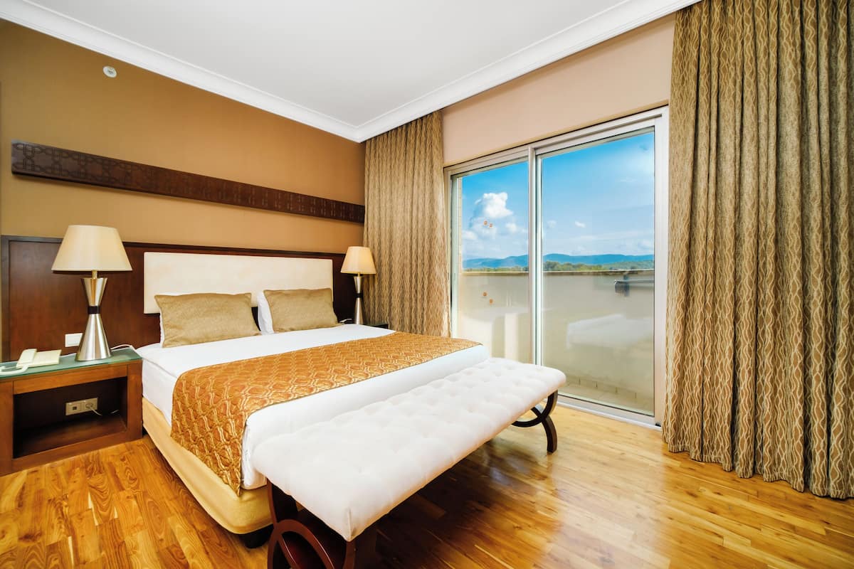 Habitación de hotel con una cama grande, dos lámparas de noche, una mesita de noche de madera y vista a un cuerpo de agua a través de una puerta corrediza de vidrio.