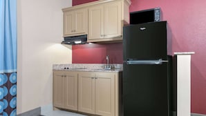 A compact kitchen with beige cabinets, a black refrigerator, and a microwave on top.