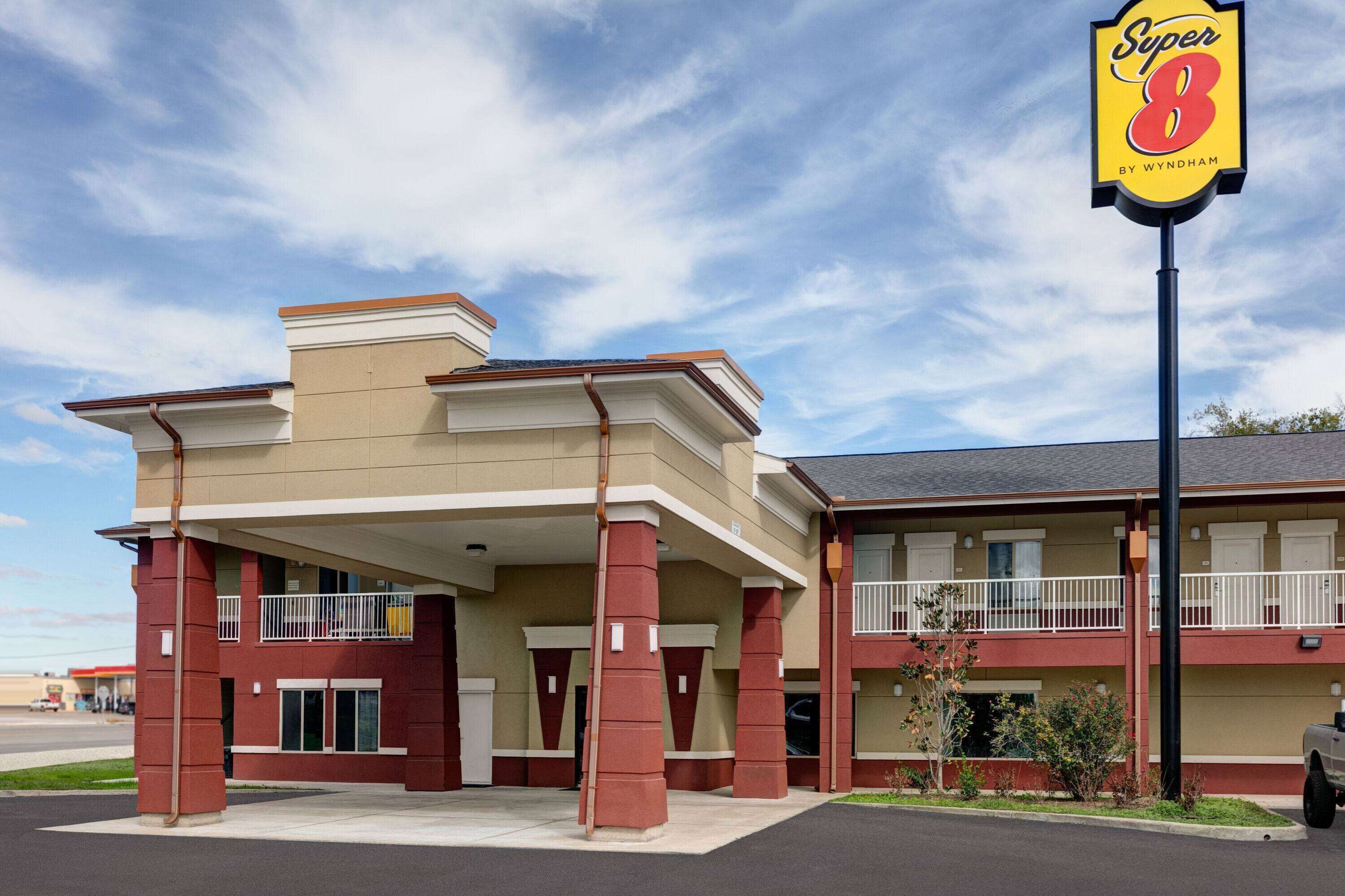 Un motel de dos pisos con fachada beige y roja, un acceso cubierto y un letrero que dice 'Super 8 by Wyndham'.