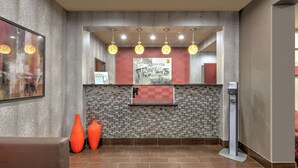 A reception area with a check-in counter, a large framed poster, and two orange vases.