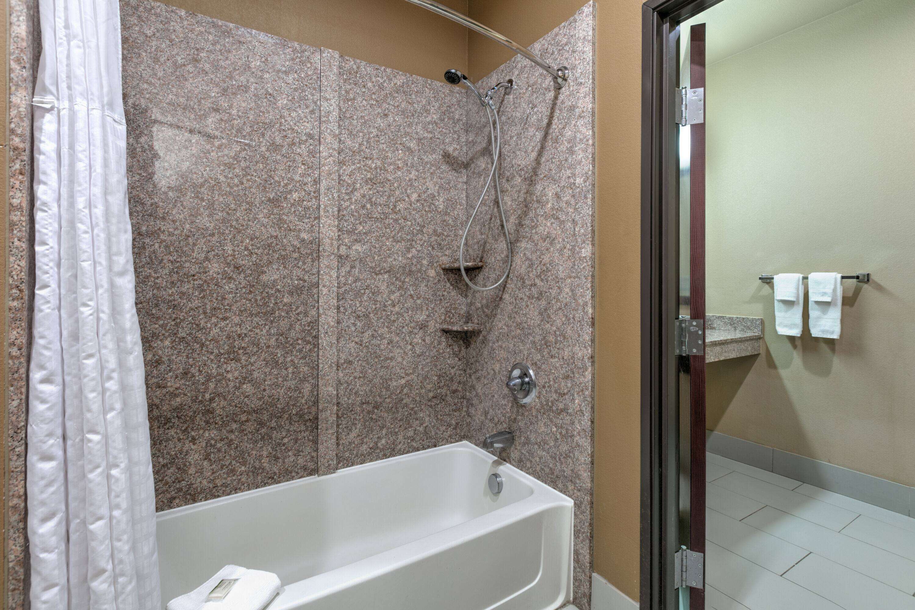 A bathroom with a shower, a bathtub, and a glass door leading to a hallway.