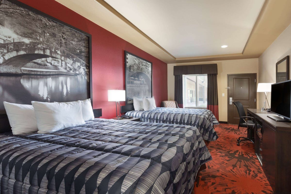A hotel room with two beds, a desk, a TV, and a large window.