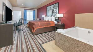 A hotel room with a bed, desk, chair, TV, and a bathroom with a bathtub.