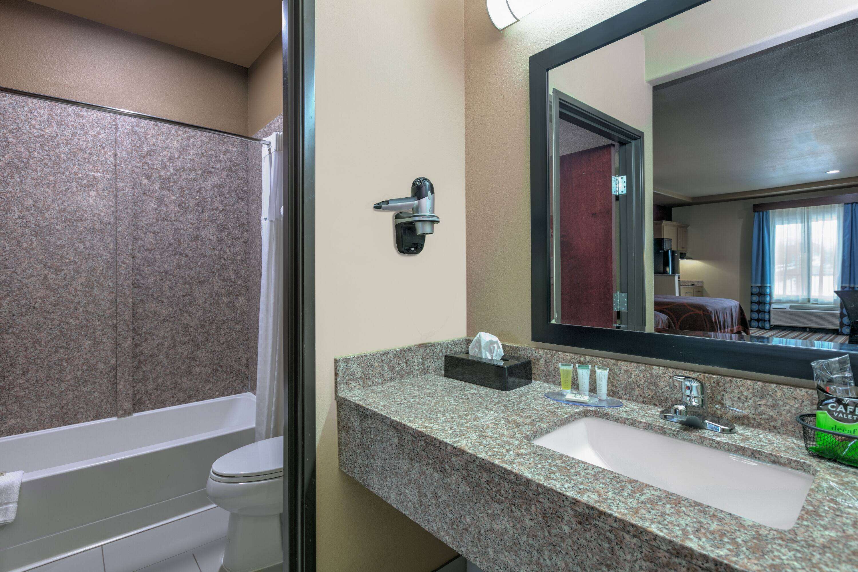Un baño con encimera de granito, lavabo, espejo y ducha.