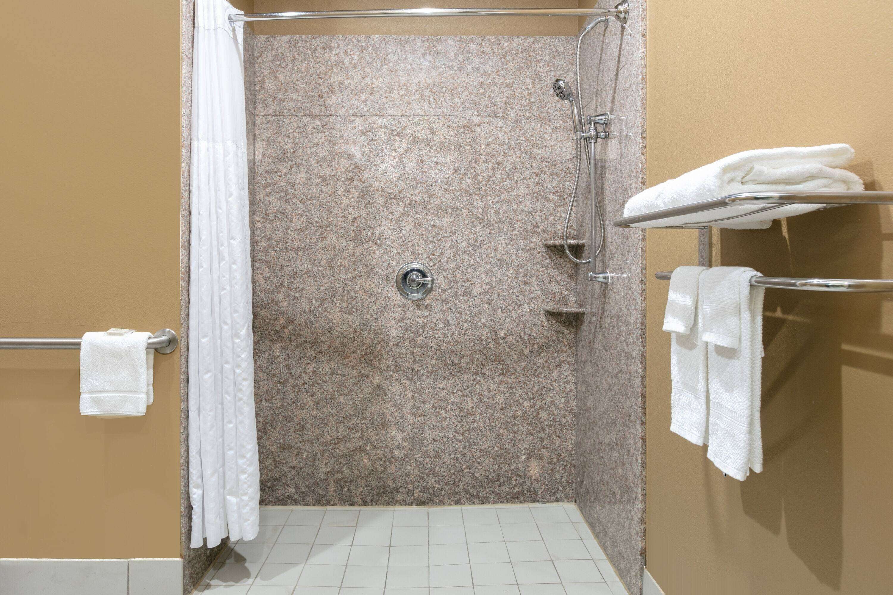 A shower area with a granite wall, a towel rack with folded towels, and a showerhead.