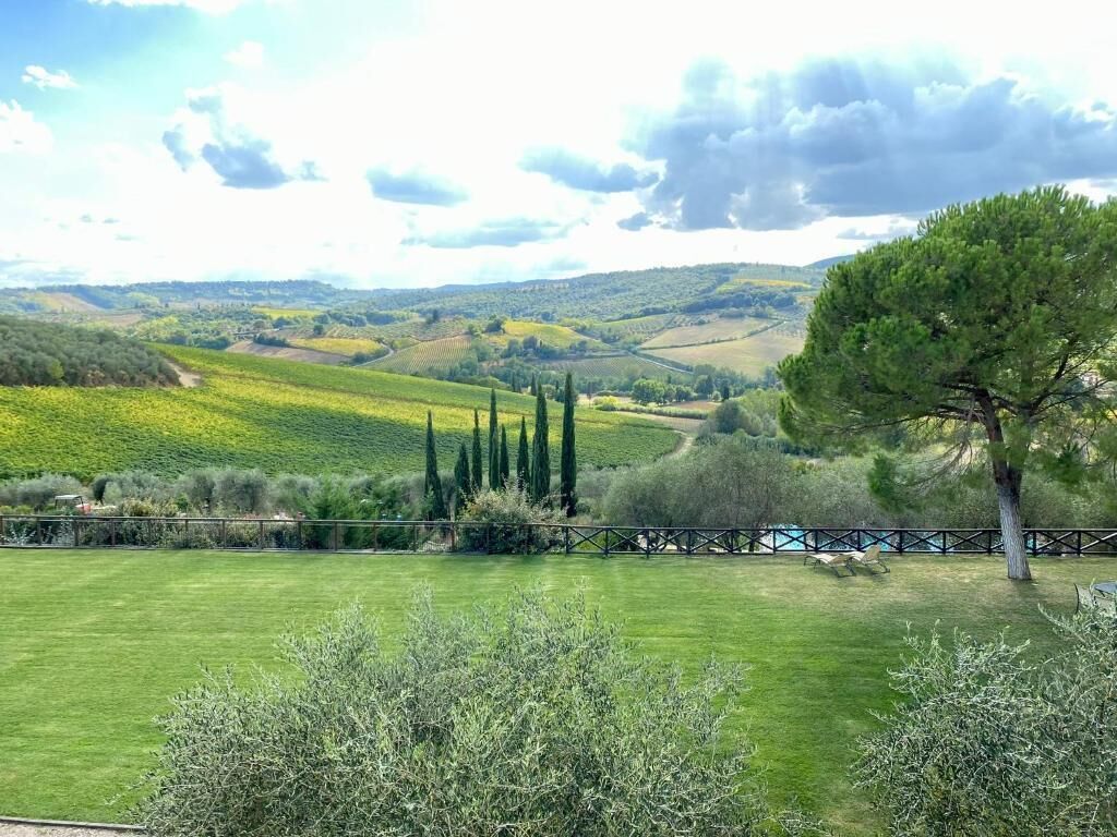 Paisaje rural con colinas onduladas, cielo despejado y una cerca en primer plano.