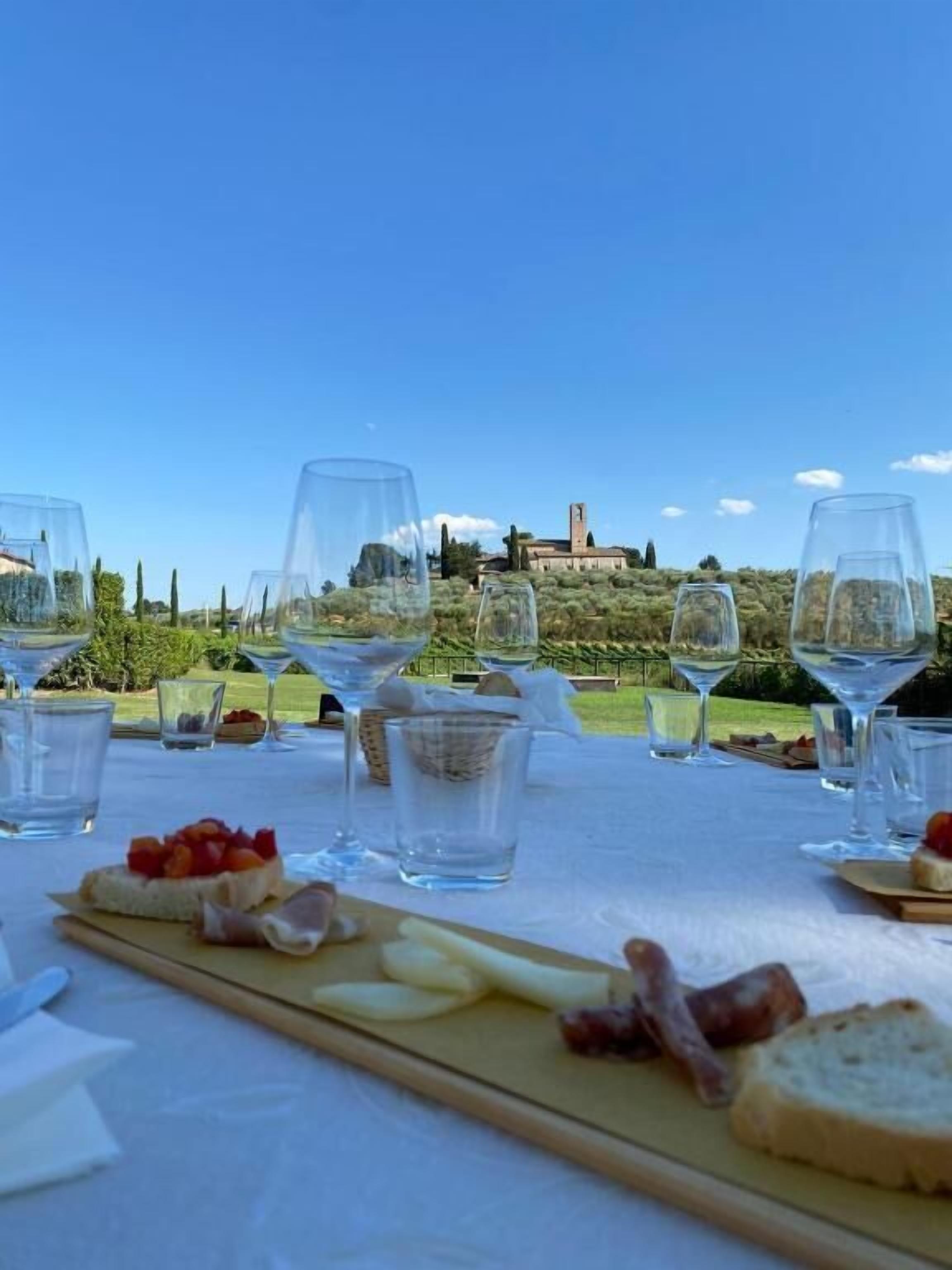 A table set with wine glasses, a wooden board with cheese and meats, and a view of a building in the distance.