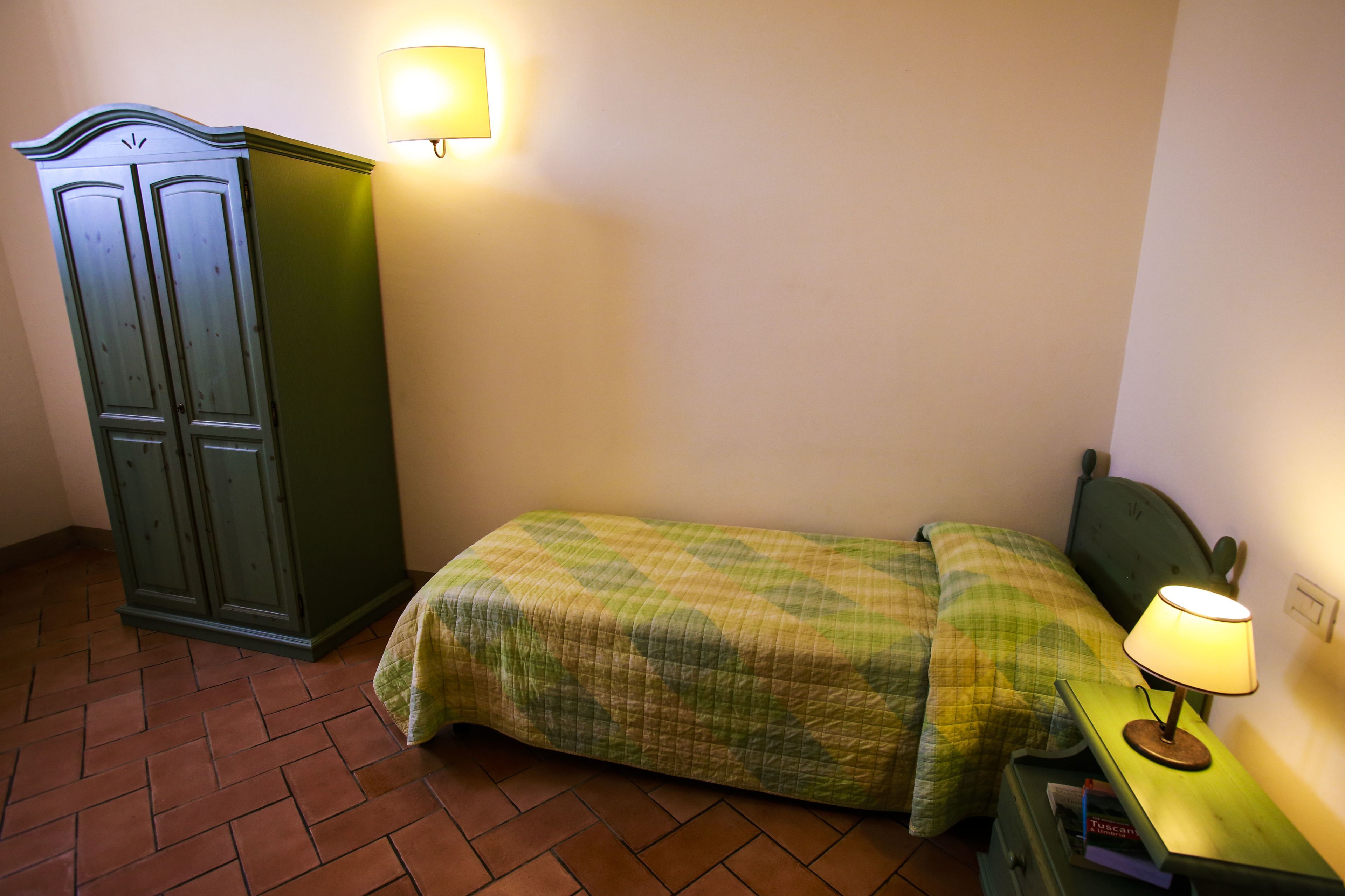 A small bedroom with a bed, a nightstand, a lamp, and a wardrobe.