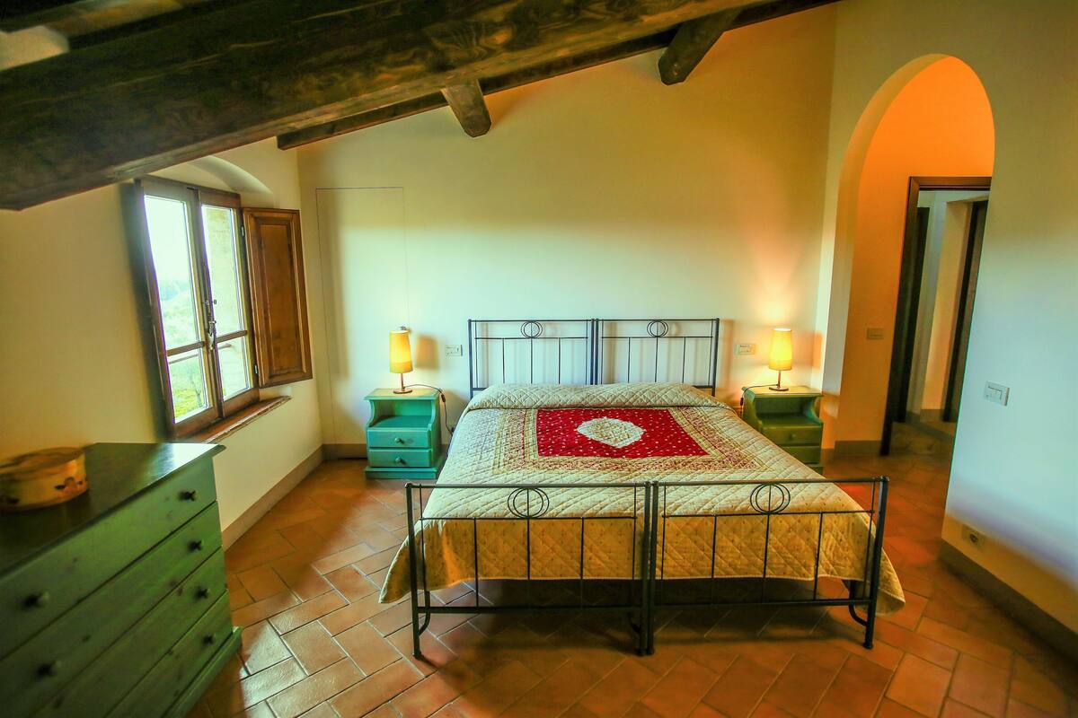 Ein Schlafzimmer mit einem Bett, zwei Nachttischen mit Lampen, einer Kommode und einem Fenster mit Blick.
