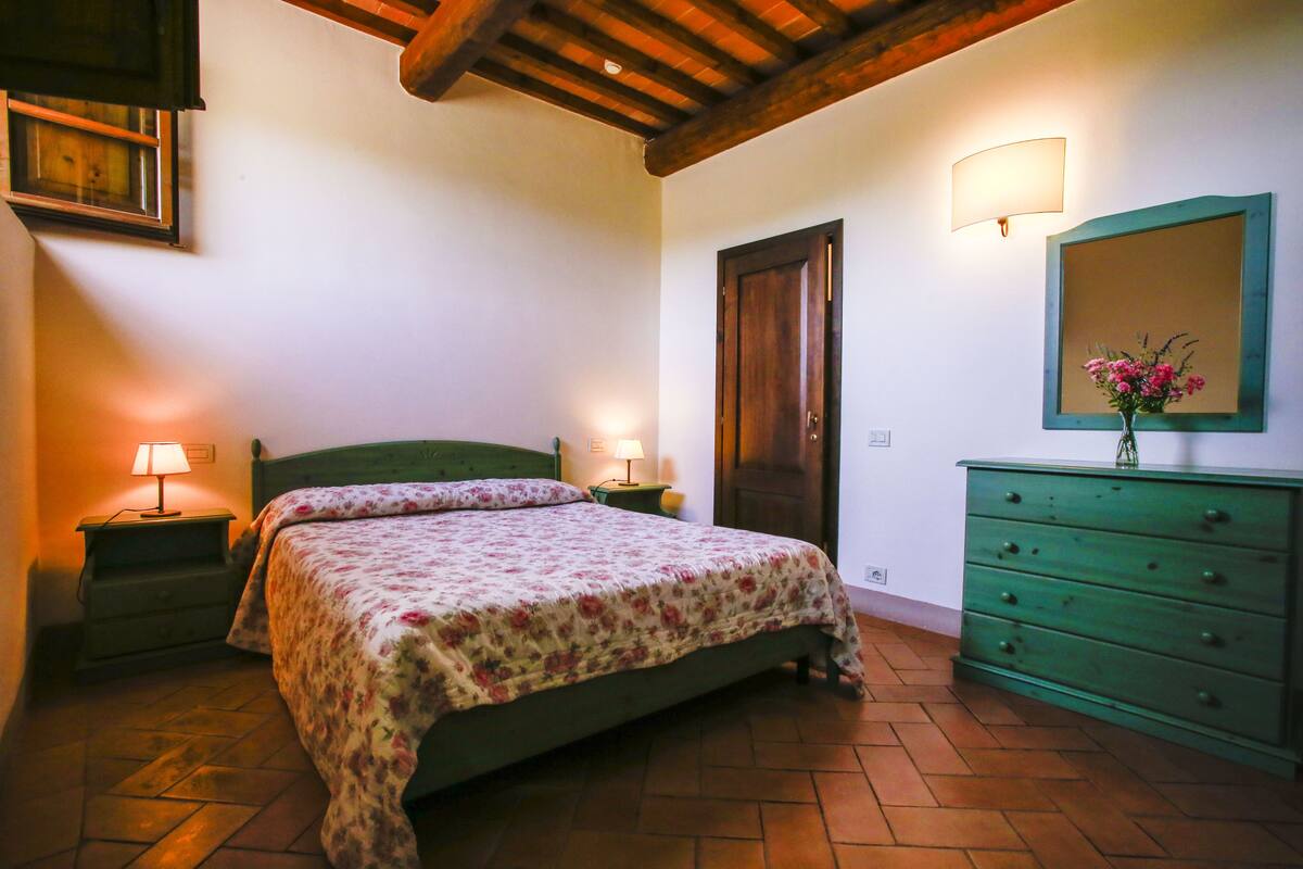 Ein Schlafzimmer mit einem Bett, einem Schminktisch, einem Spiegel, einer Lampe und einer Tür.