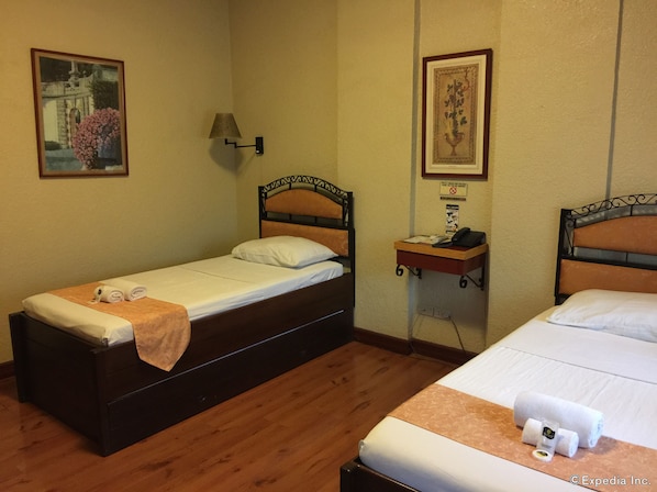 Habitación de hotel con dos camas individuales, una mesita de noche con lámpara y dos cuadros en las paredes.