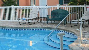A pool area with lounge chairs and a white fence.