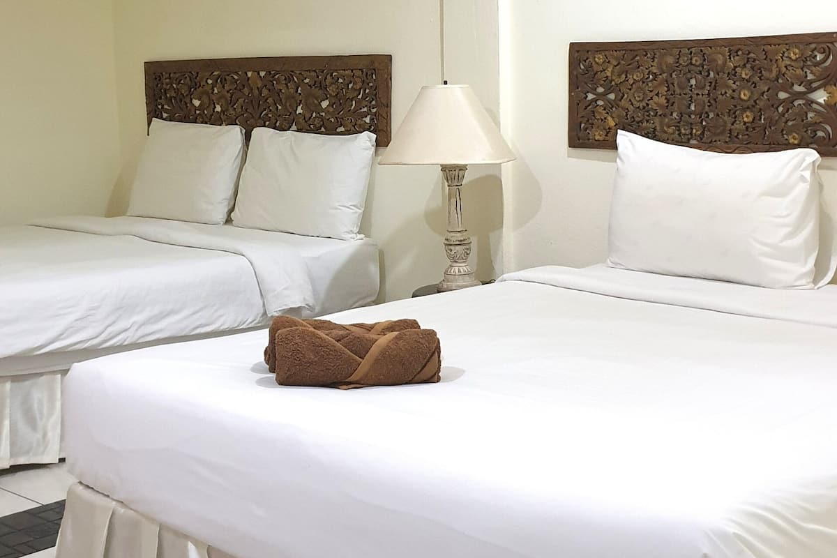 Une chambre d’hôtel avec deux lits simples, une table de chevet avec une lampe et une tête de lit décorative.