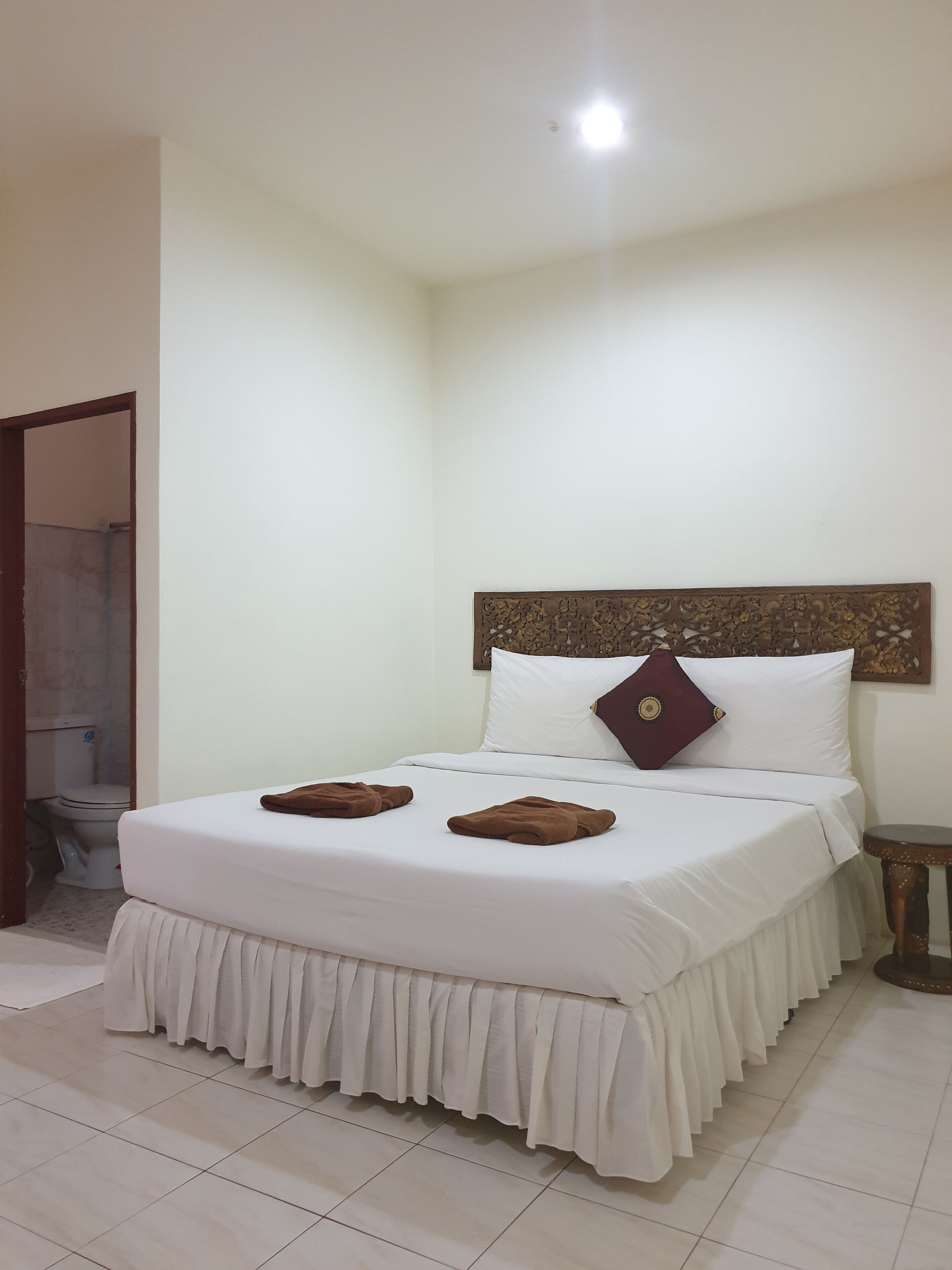 A neatly made bed with white bedding and a decorative headboard, a small bedside table, and a visible bathroom door.