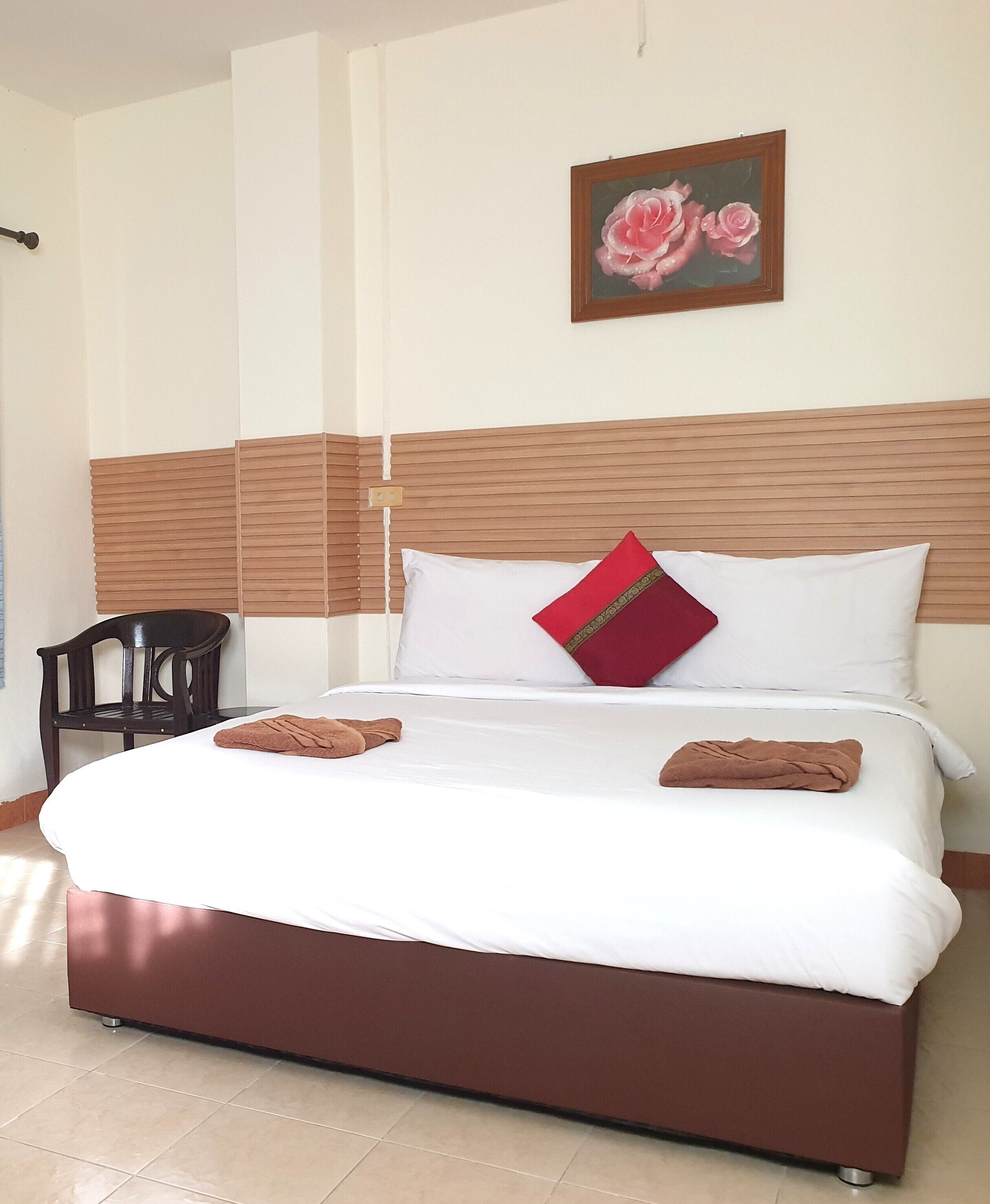 A neatly made bed with white and brown bedding, a red pillow, and two brown towels.