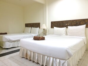 Habitación de hotel con dos camas, cada una con ropa blanca y un cabecero decorativo. Una toalla marrón está colocada en la cama en primer plano.