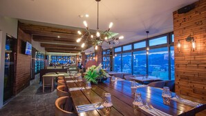 A modern dining area with a long wooden table set for a meal, large windows offering a view of the city, and a unique chandelier. - Hotel XYZ (Tacloban)
