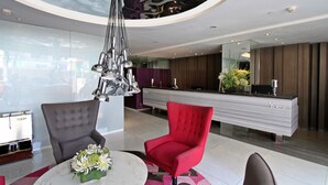 A modern lobby with a reception desk, a red chair, a grey chair, and a round table with a flower arrangement. - Hotel XYZ (Tacloban)