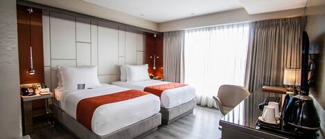Une chambre d’hôtel avec deux lits, un bureau, une chaise, une télévision et une fenêtre avec des rideaux.