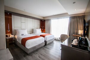 Habitación de hotel con dos camas, un escritorio, una silla, un televisor y una ventana con cortinas.