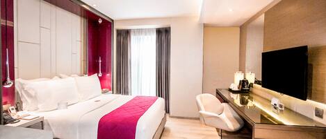 A modern hotel room with a large bed, a desk with a flat-screen TV, and a chair.