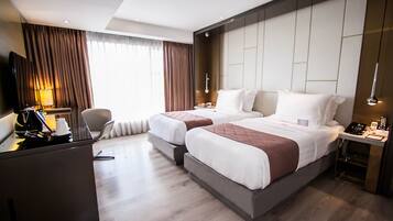 A hotel room with two beds, a desk with a lamp, a chair, and a TV.