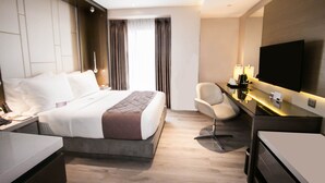 A modern hotel room with a large bed, a desk with a chair, a flat-screen TV, and a large window with curtains. - Hotel XYZ (Tacloban)