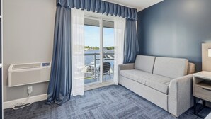 Una habitación con sofá, una mesita, una ventana con cortinas y vista a un puerto deportivo.
