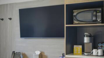 Une chambre d’hôtel moderne équipée d’une télévision à écran plat, d’un four à micro-ondes, d’une machine à café, d’un mini-réfrigérateur et d’une chaise jaune.