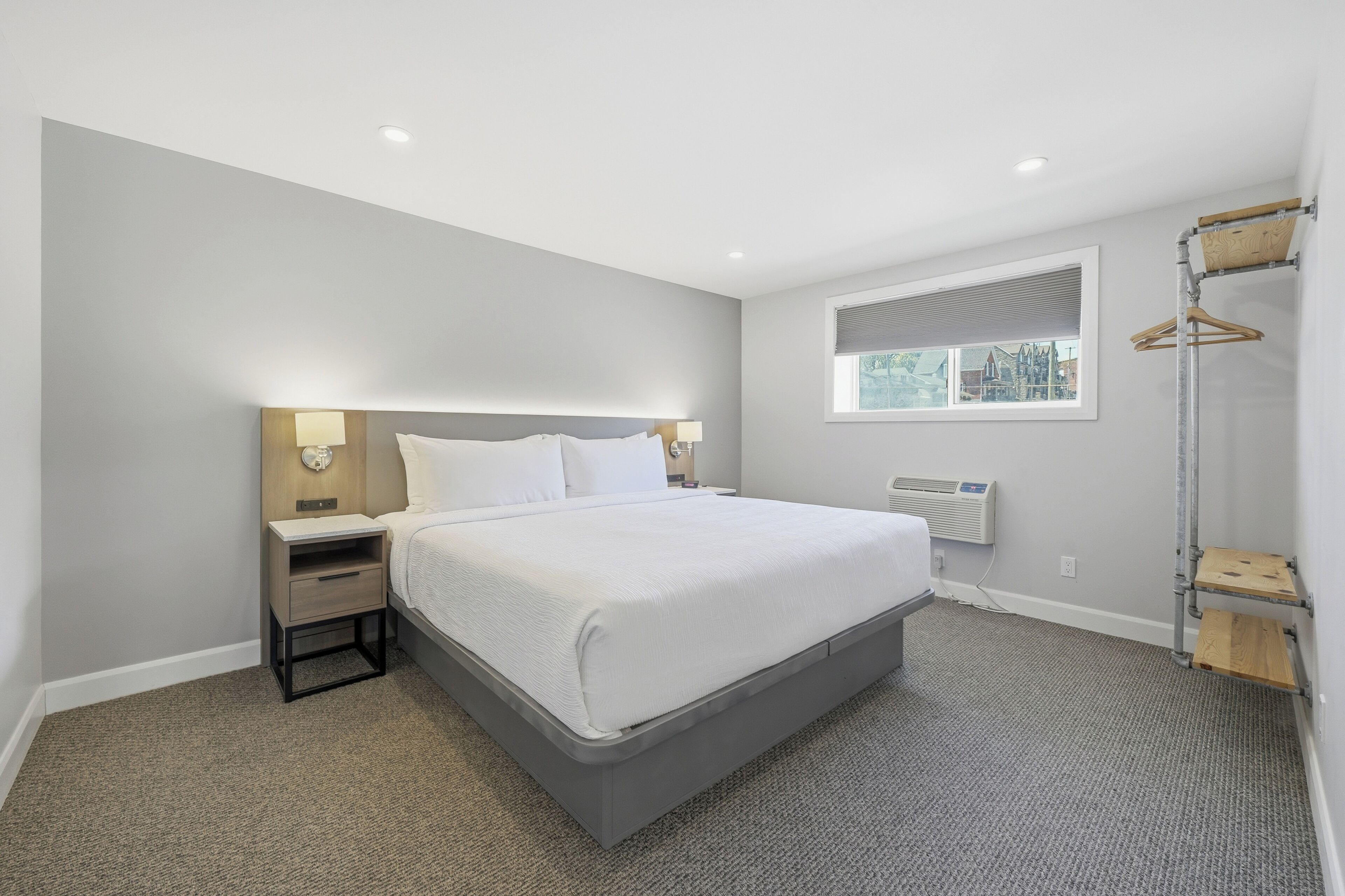 A modern hotel room with a large bed, bedside tables, a window with blinds, and a built-in heater.