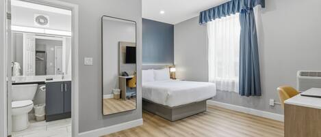 A modern hotel room with a bed, bedside table, and a desk.