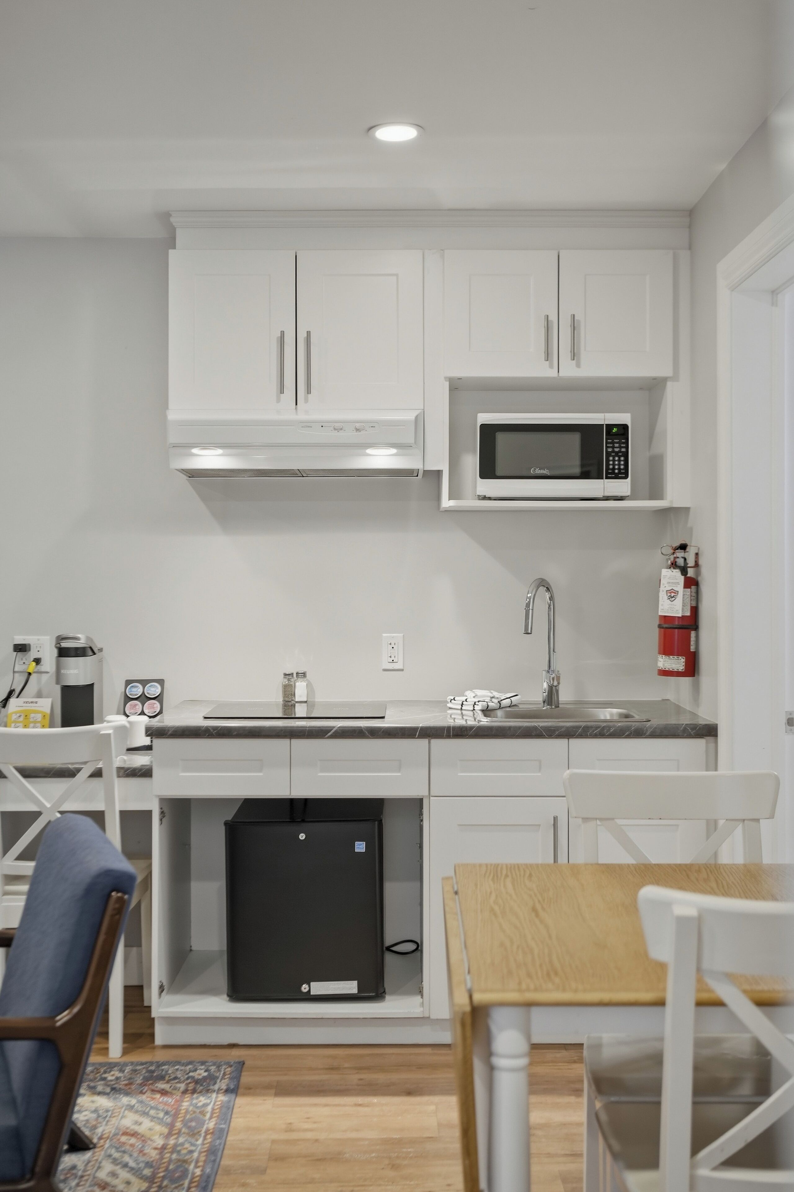 Una cocina compacta con armarios blancos, un microondas, un lavamanos y un refrigerador pequeño.