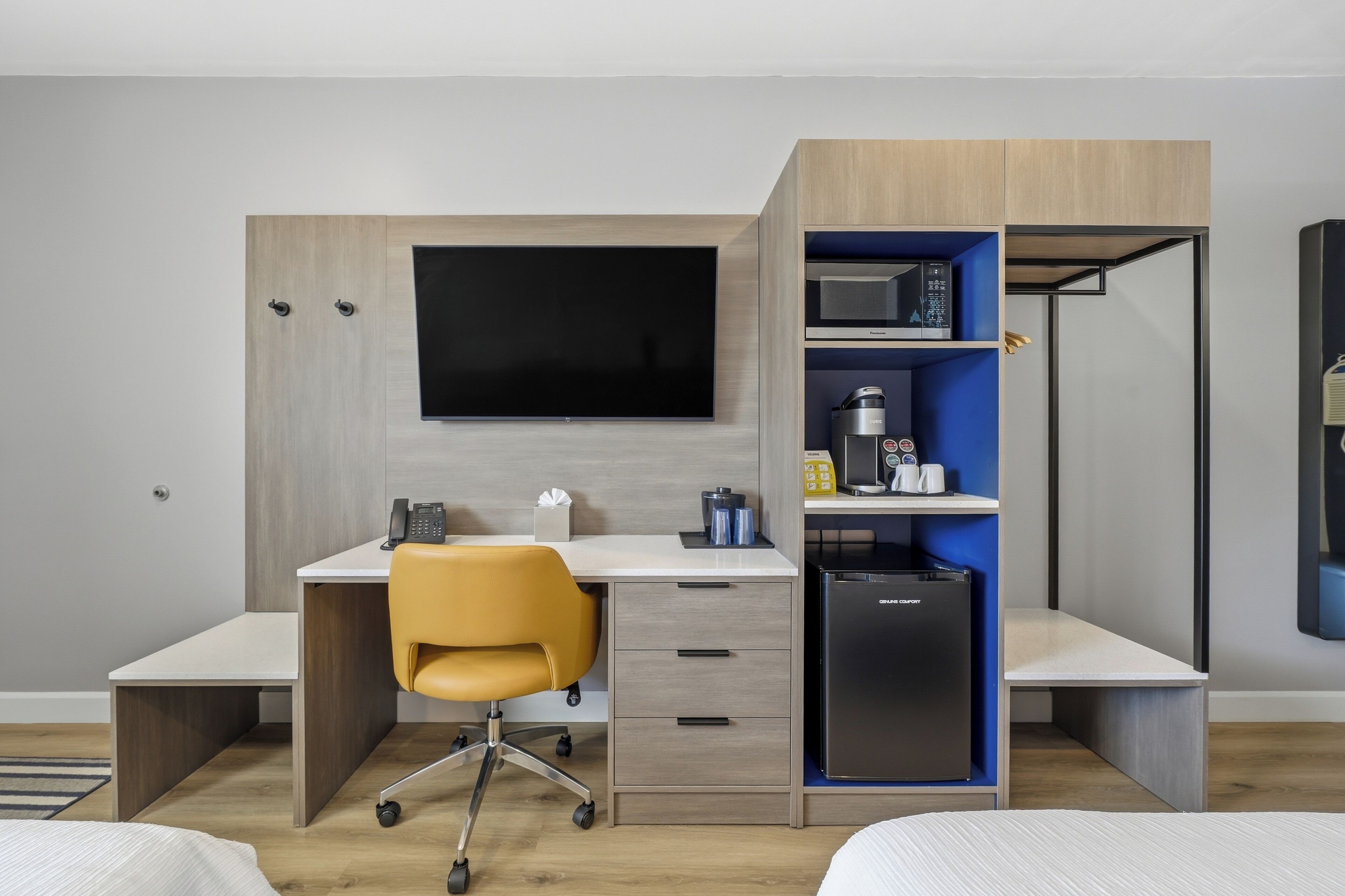 A modern hotel room with a flat-screen TV, a desk with a chair, a mini-fridge, and a microwave.