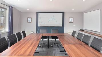 A conference room with a long wooden table, black office chairs, and a large screen displaying a graph.