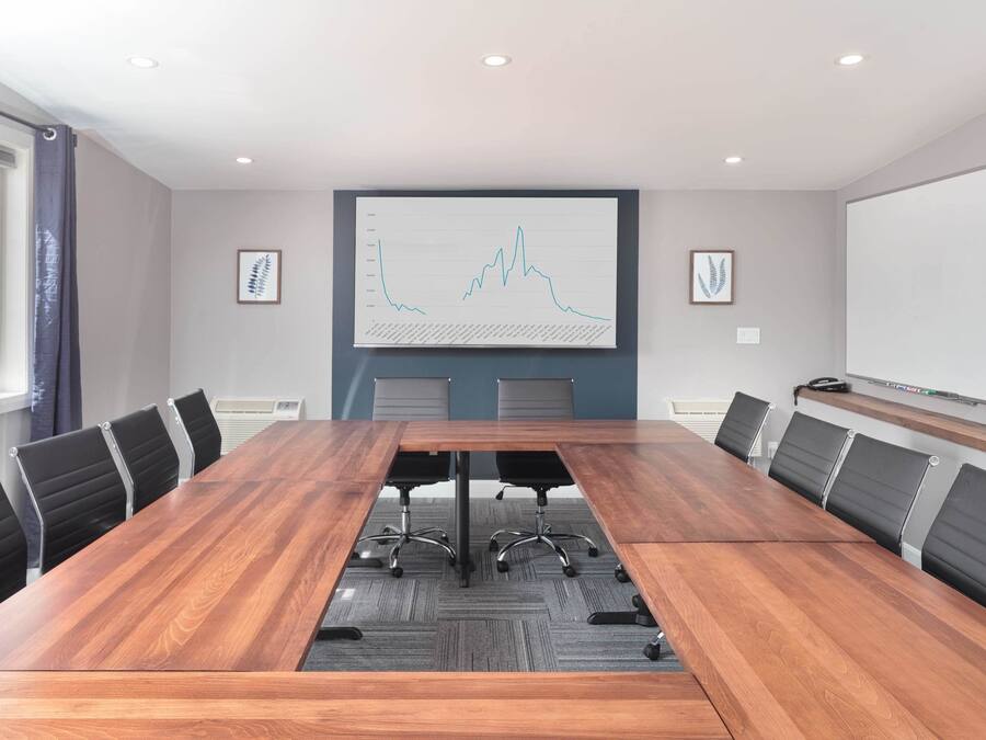A conference room with a long wooden table, black office chairs, and a large screen displaying a graph.