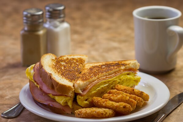 A plate with a grilled sandwich, fried items, and a cup of coffee.