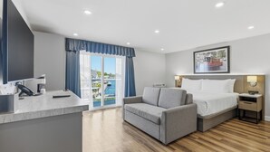 Habitación de hotel con cama, sofá, escritorio y teléfono, y ventana con vista al mar.