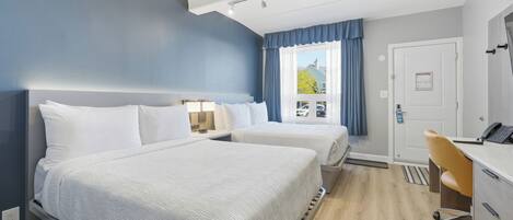 Una habitació d'hotel amb dos llits, un escriptori, una cadira, una finestra amb cortines i una porta amb un rètol.