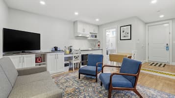 Un salon moderne avec un téléviseur à écran plat, un canapé gris, des fauteuils bleus et un tapis à motifs.