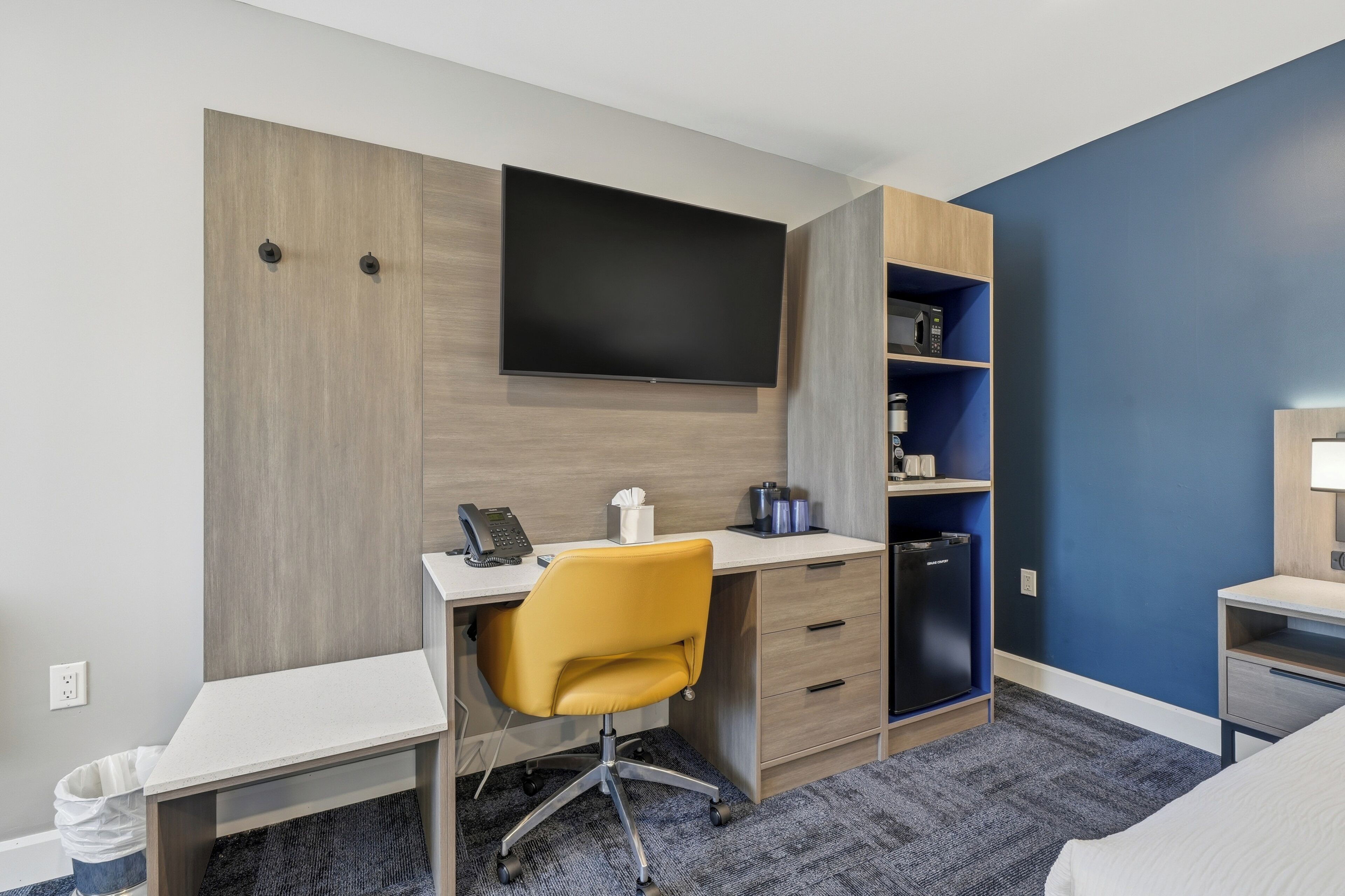 Habitación de hotel con escritorio, silla, televisor, minibar y cama.
