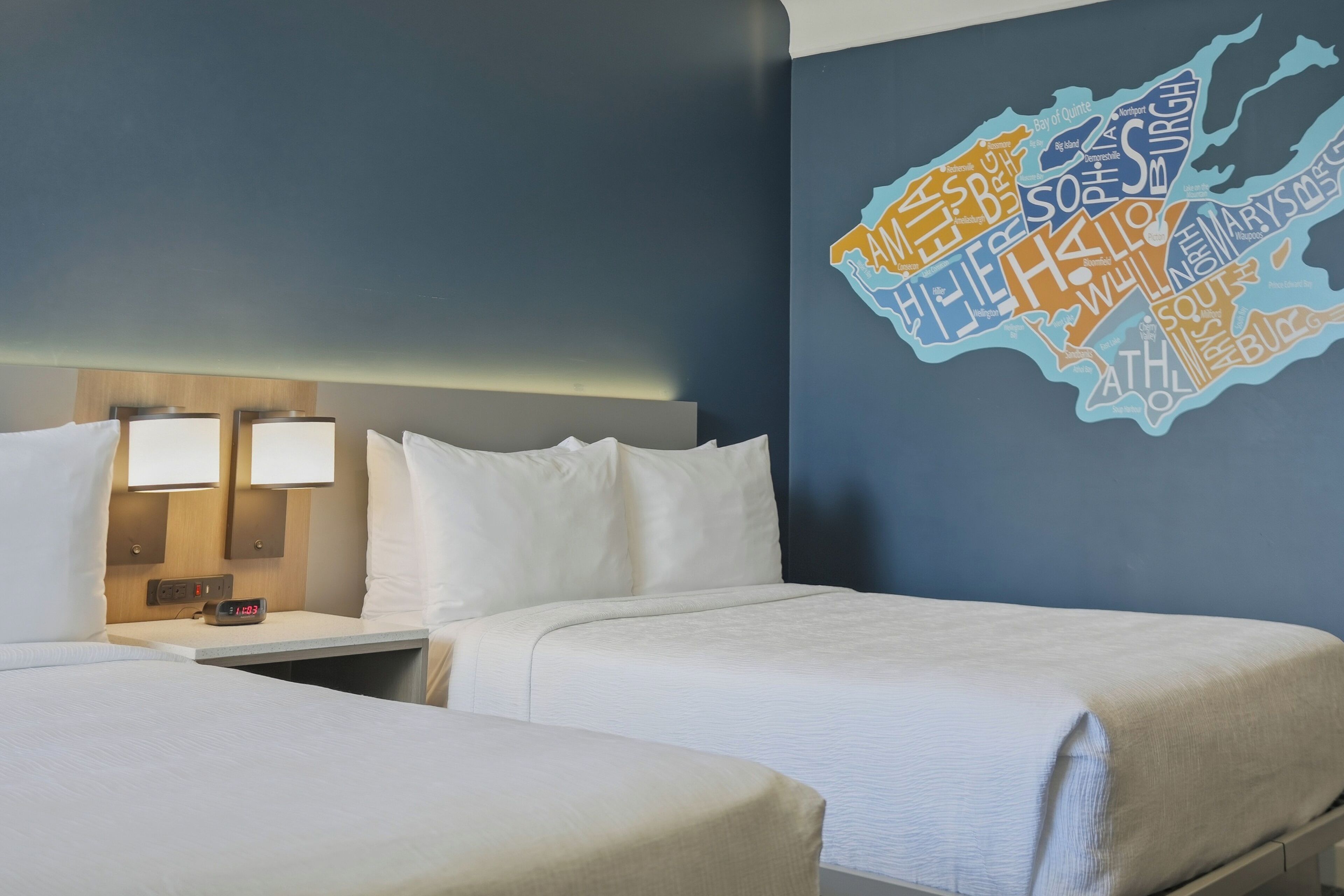 Une chambre d’hôtel avec deux lits, une table de chevet avec une horloge et une carte murale.