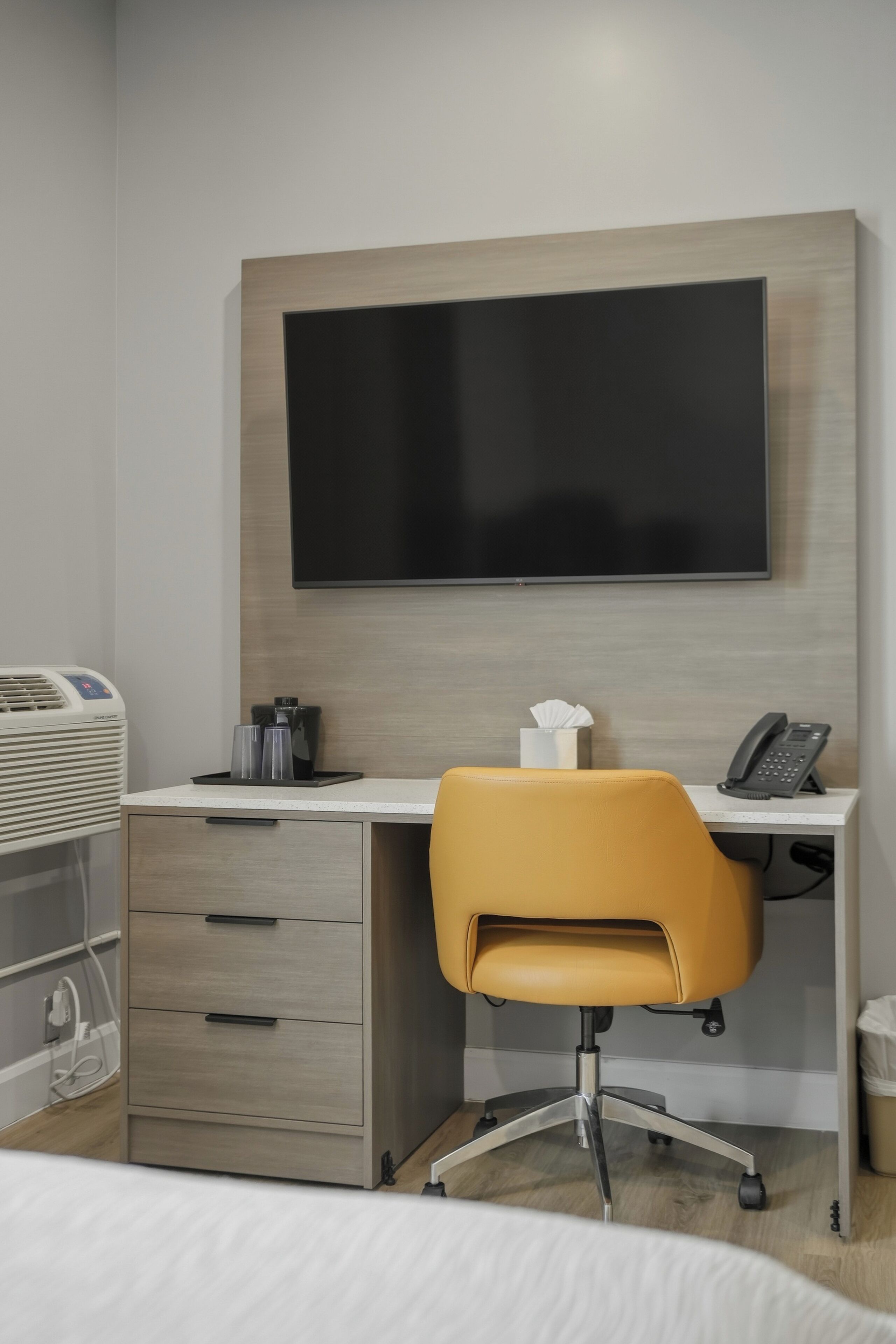Une chambre d’hôtel comprenant un lit, un bureau avec une chaise, un téléviseur à écran plat, une machine à café, un téléphone et une poubelle.