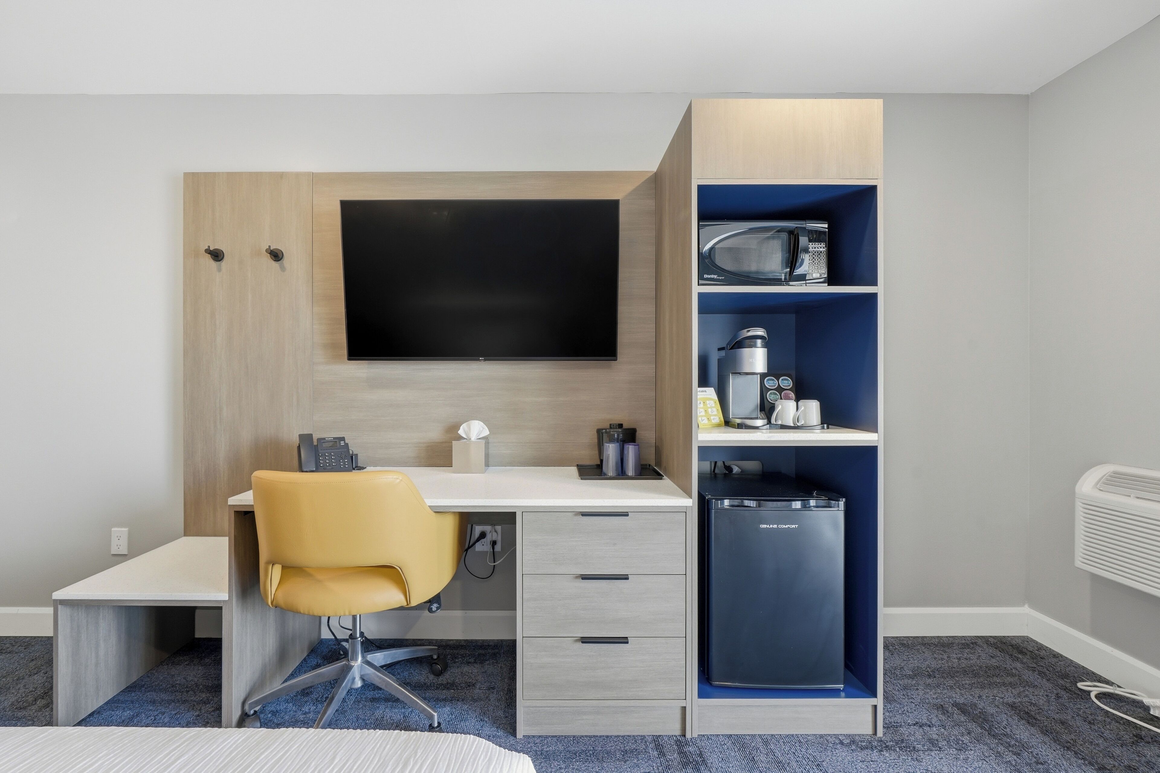 Hotellihuone, jossa on työpöytä, tuoli, televisio, mikroaaltouuni, minijääkaappi ja sänky.
