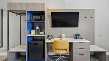 A compact hotel room with a kitchenette, a desk with a chair, a flat-screen TV, and a wardrobe.