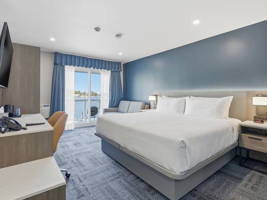 Une chambre d’hôtel équipée d’un lit, d’un bureau, d’une chaise, d’une table de chevet et d’un téléviseur fixé au mur.